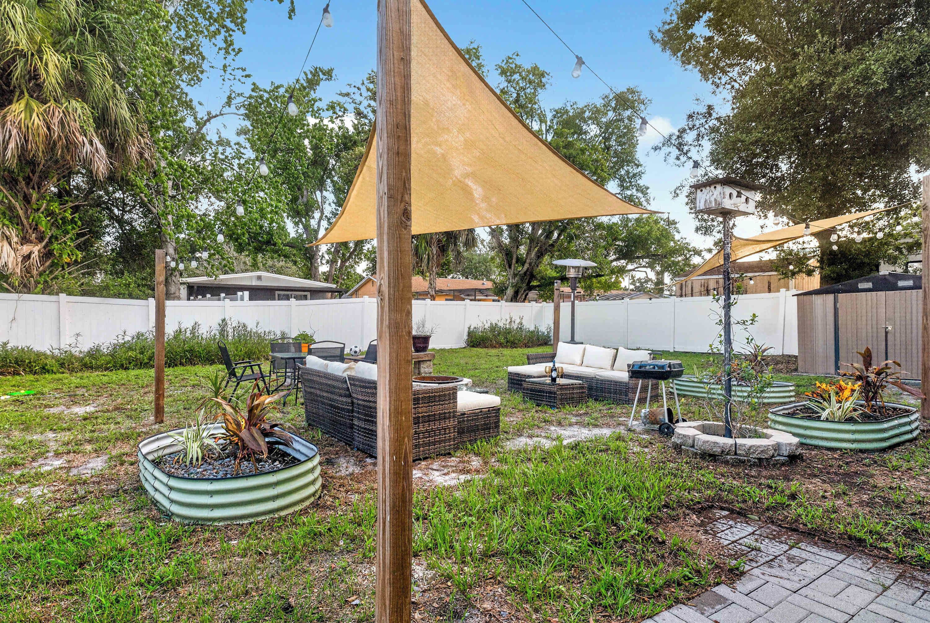 Een terras buiten met een houten tafel, rieten meubels en plantenbakken.
