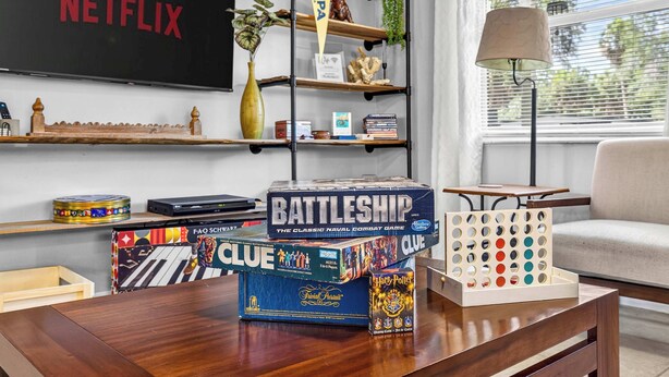 A living room with a Netflix TV, a coffee table with board games, and a bookshelf. - The Landing Pad | Pet Friendly Yard (Tampa)