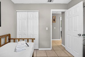 Une chambre à coucher avec un lit, une tête de lit en bois, une porte blanche et un couloir menant à une autre pièce.