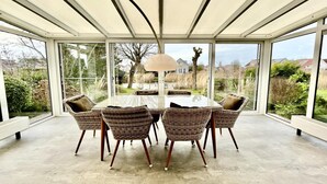 Ein Wintergarten mit Glastisch und Korbstühlen, der einen Ausblick ins Freie bietet.