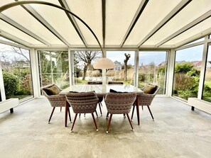 Ein Wintergarten mit Glastisch und Korbstühlen, der einen Ausblick ins Freie bietet.