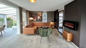Ein modernes Wohnzimmer mit einer Eckcouch, einem Glastisch, einem grünen Sessel, einem Kamin und einem an der Wand befestigten Fernseher.
