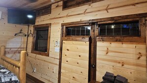 A wooden interior with a bed, a wooden door, and a window.