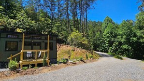 A cabin with a deck and a gravel driveway leading into a forest.
