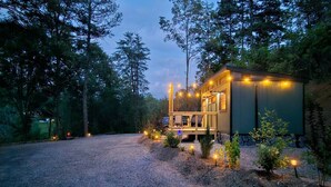 Una cabaña con porche, rodeada de árboles e iluminada con luces colgantes.