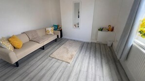 Una sala de estar con sofá, alfombra, espejo y repisa con juguetes.