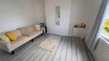 A living room with a sofa, a rug, a mirror, and a shelf with toys.