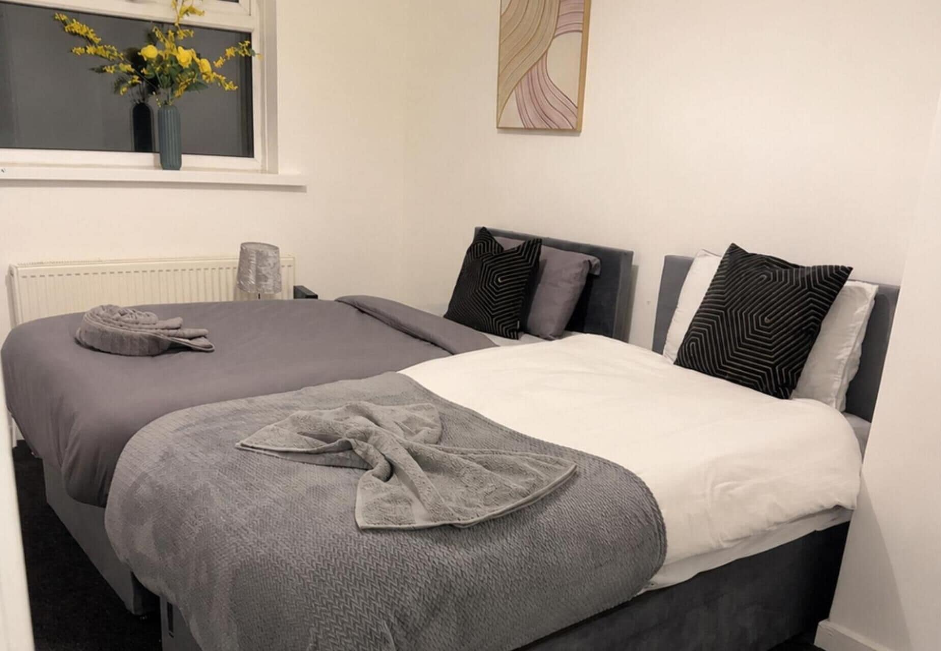 Ein Schlafzimmer mit zwei Betten, einem Heizkörper, einem Fenster mit Blick und einem Wandbild.