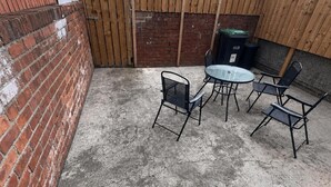 Un patio con un muro de ladrillo, un portón de madera y una mesa redonda con cuatro sillas.
