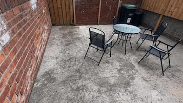 A patio area with a brick wall, a wooden gate, and a round table with four chairs.