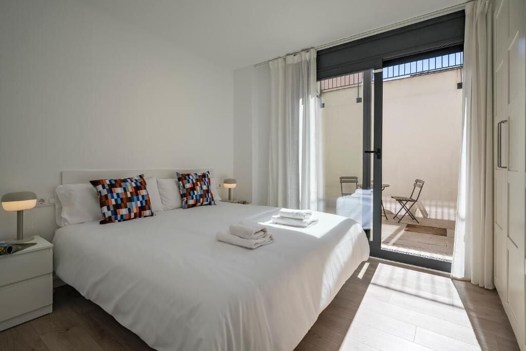A hotel room with a large bed, a nightstand, a lamp, and a view of the balcony.
