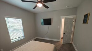 Ein Schlafzimmer mit einem Bett, Deckenventilator, Fernseher und einer Tür.