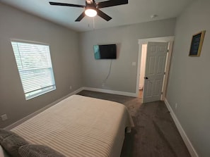 A bedroom with a bed, a ceiling fan, a TV, and a door. - Newly Built Denison White House Stay - EV Ch (Denison)