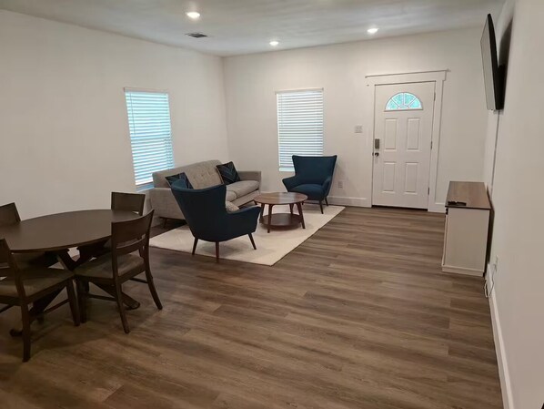 A living room with a sofa, two armchairs, a coffee table, and a dining table with chairs.