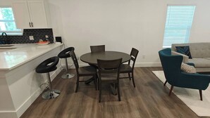 Eine moderne Küche mit weißen Schränken, einer schwarzen Spritzschutzwand und einem Essbereich mit einem runden Tisch und vier Stühlen.