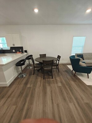 A modern kitchen with white cabinets, a black backsplash, and a dining area with a round table and four chairs. - Newly Built Denison White House Stay - EV Ch (Denison)