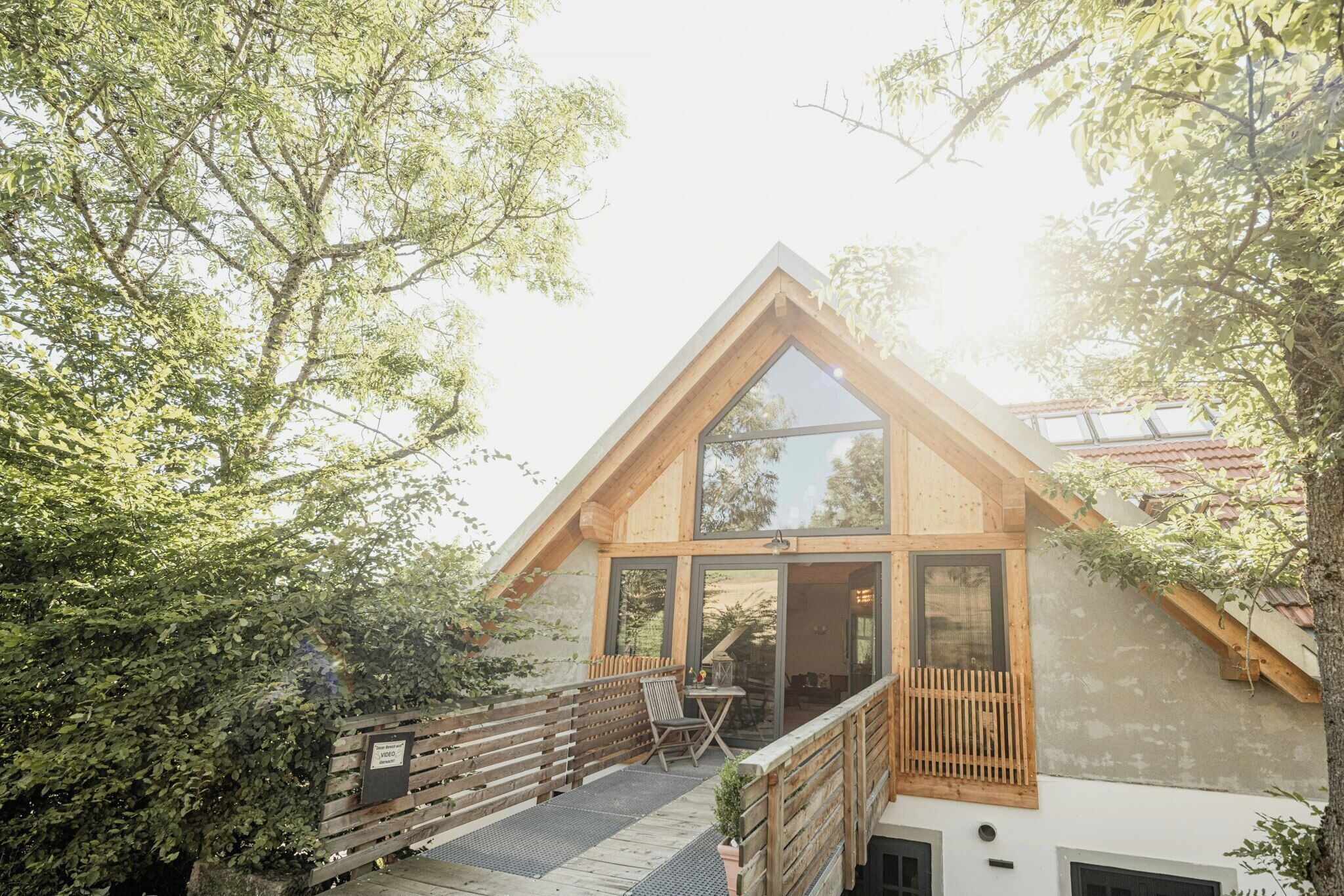 Ein modernes Haus mit Holzterrasse, großen Fenstern und einem geneigten Dach.