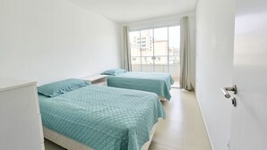 A hotel room with two beds, a window with curtains, and a door with a handle. - La Rosadita by LikeHome  (Bombinhas)