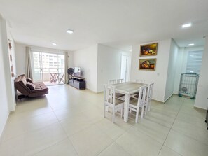 A living room with a sofa, a dining table with chairs, a TV, and a painting on the wall.