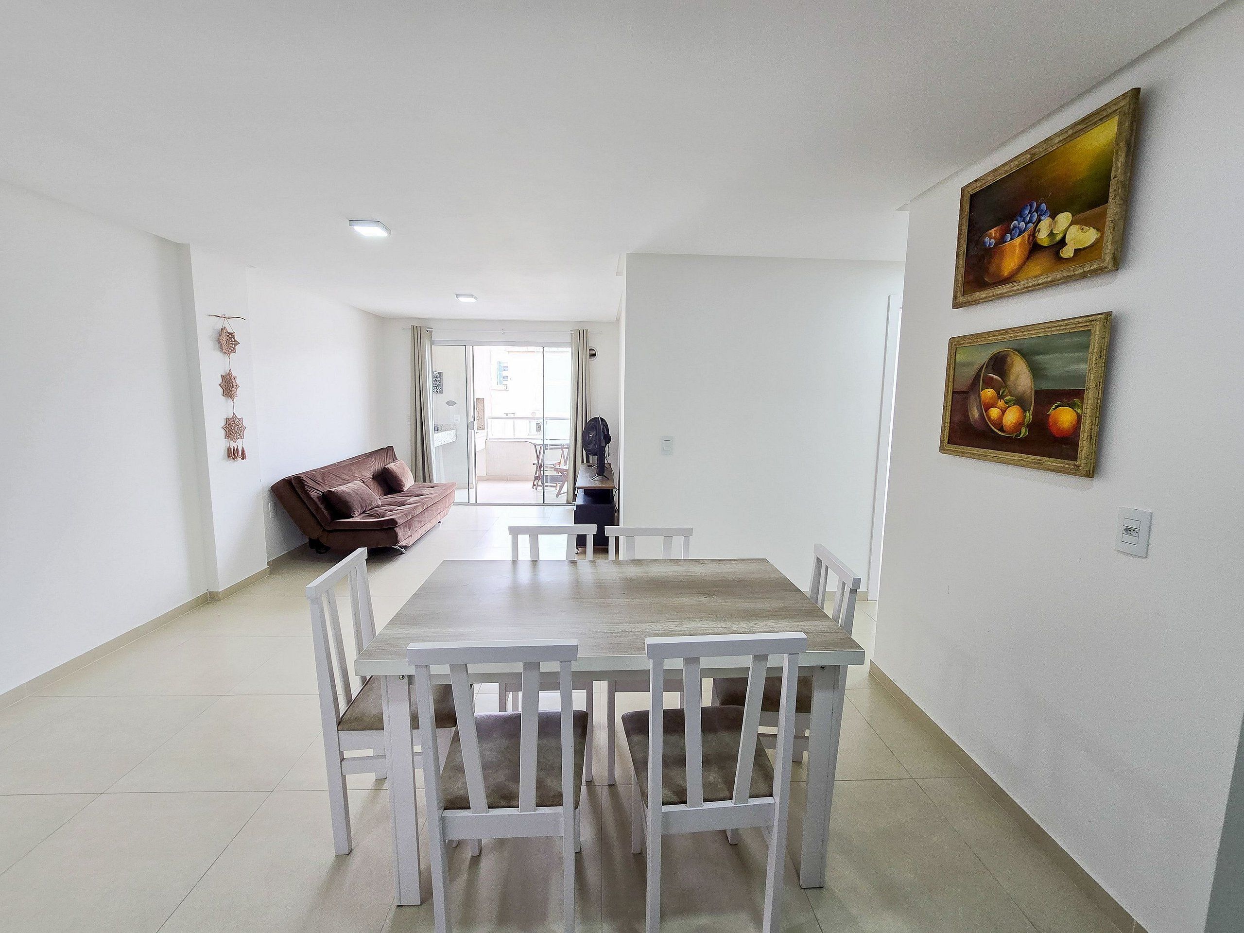 A dining area with a wooden table and white chairs, a brown sofa, and a painting on the wall.