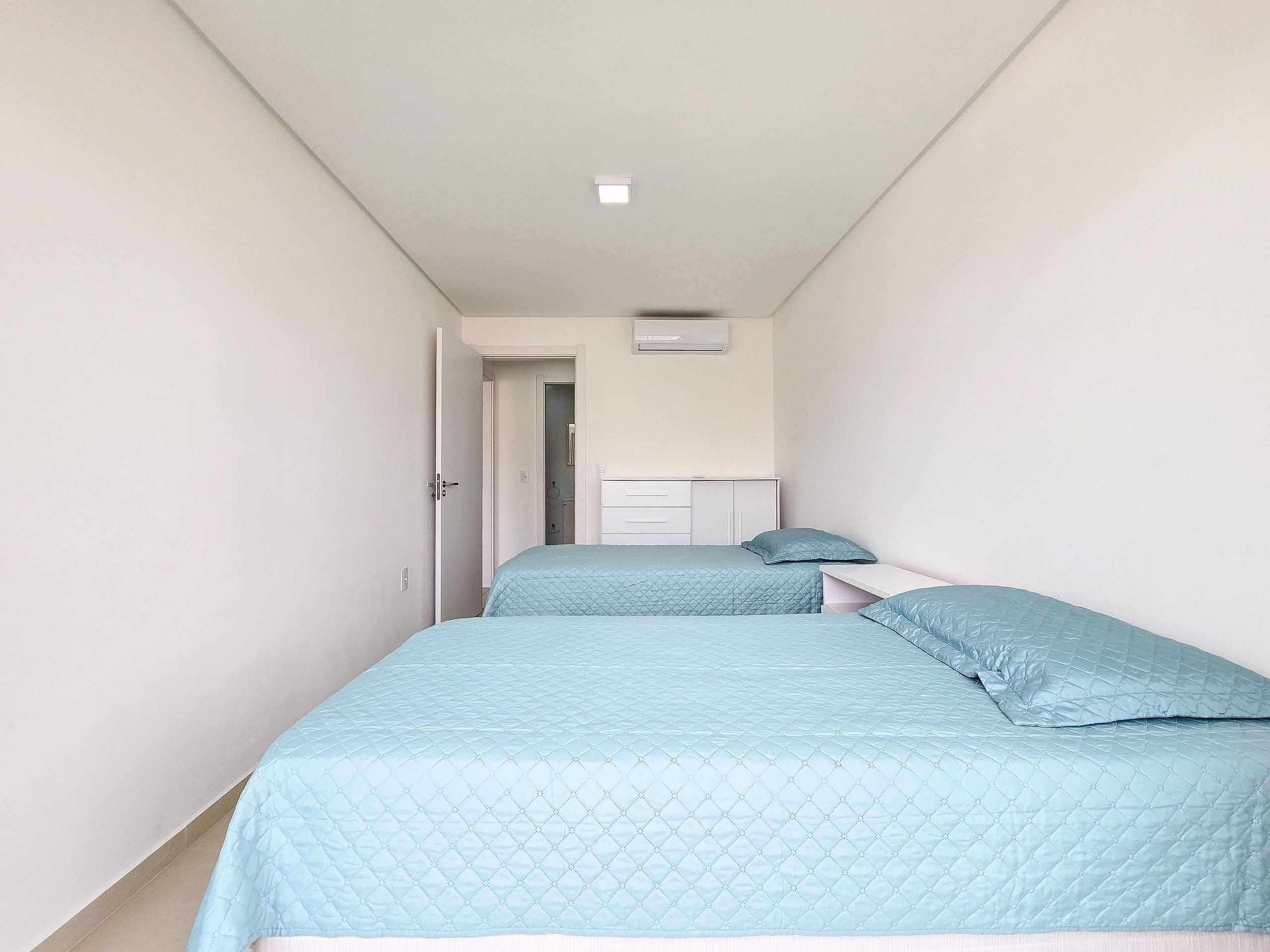 A narrow hallway with two beds, each with a blue quilted bedspread and pillows.