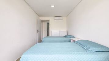 A narrow hallway with two beds, each with a blue quilted bedspread and pillows.