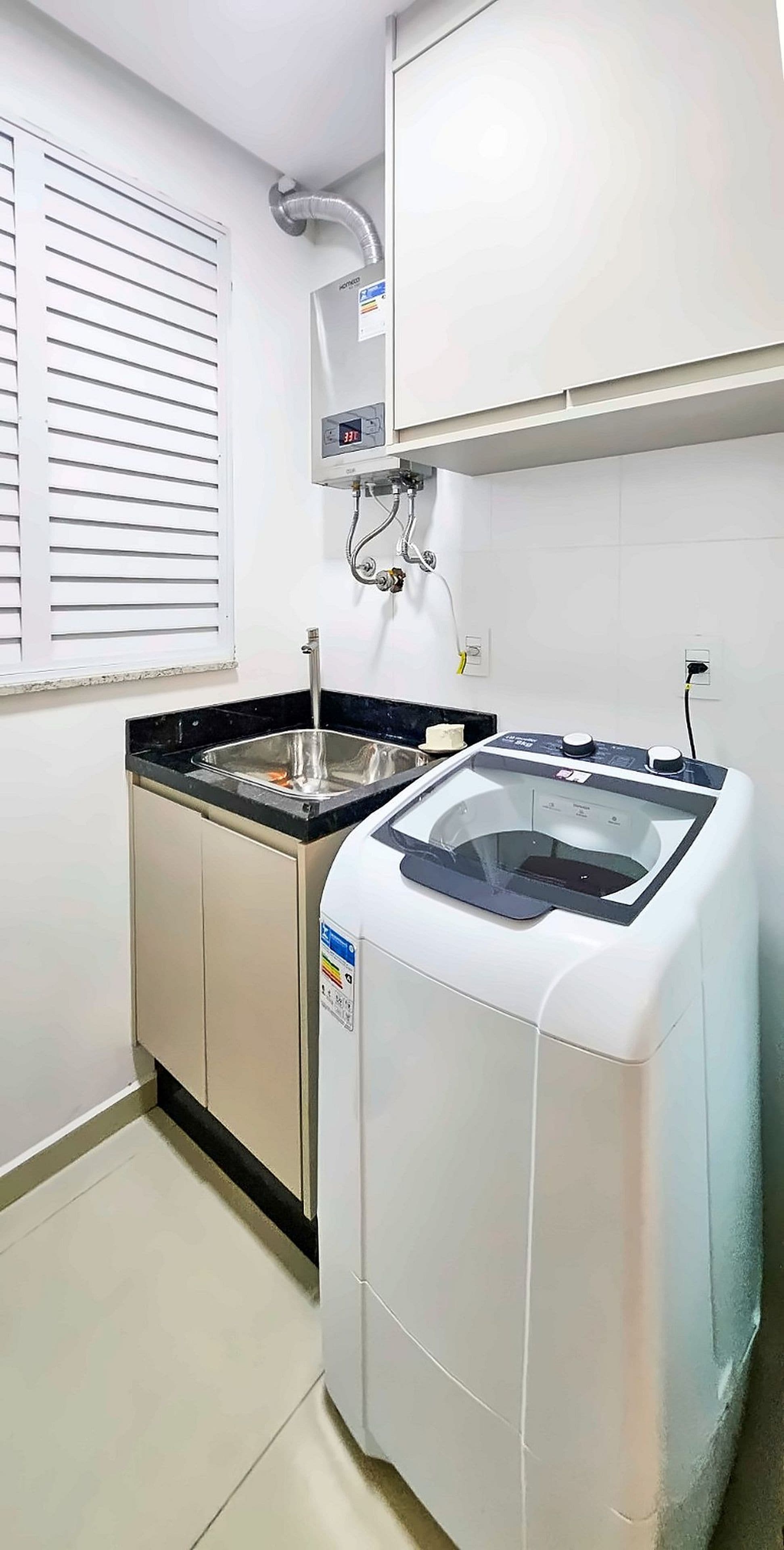 A kitchen with a built-in washer and dryer, a sink, and a window with blinds.