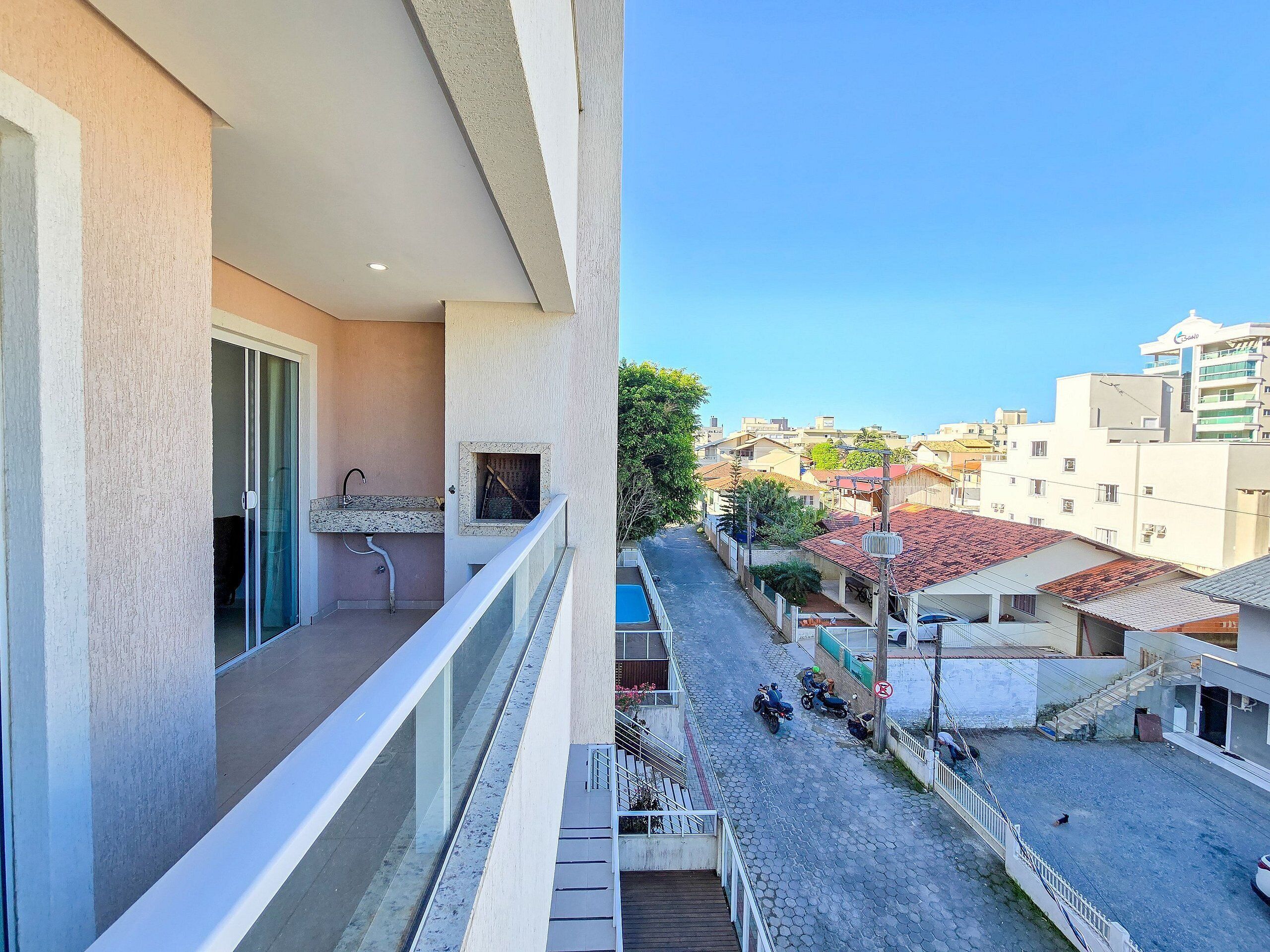 Un balcón con un lavamanos y una ventana, con vista a una calle con motocicletas estacionadas y edificios.