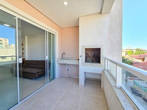 A balcony with a glass door leading to a room, a small sink, and a view of the cityscape. - La Rosadita by LikeHome (Bombinhas)