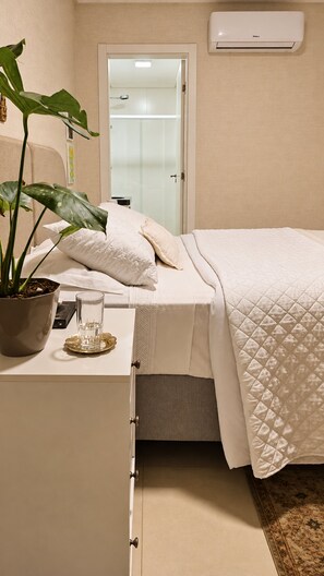 A bedroom with a bed, bedside table, potted plant, and an air conditioning unit. - La Rosadita by LikeHome  (Bombinhas)