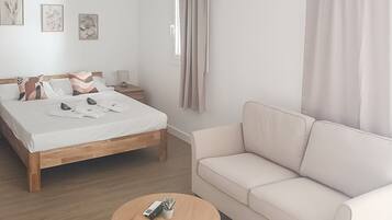 Een slaapkamer met een bed, nachtkastje, slaapbank, een ronde houten tafel en een raam met gordijnen.
