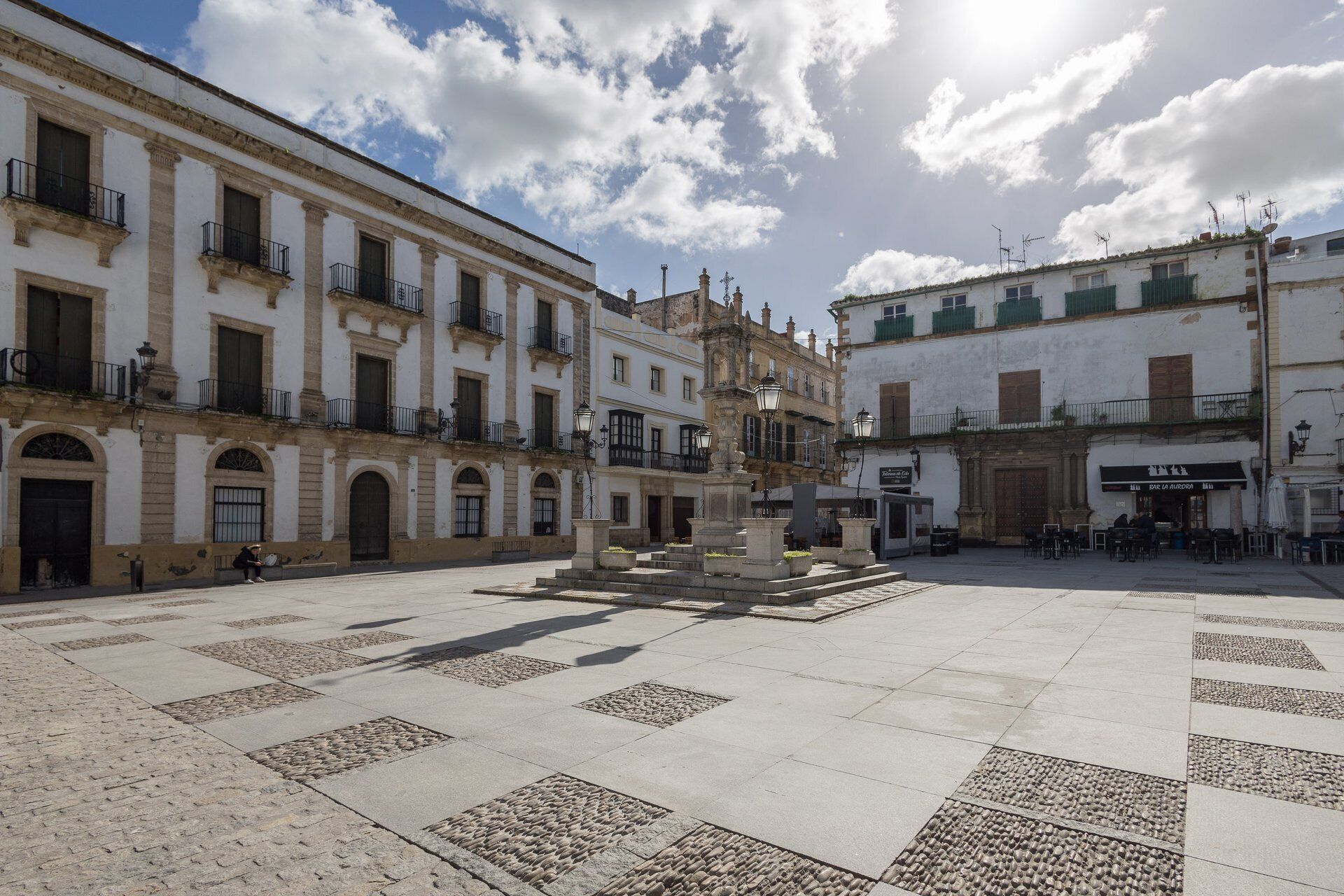 Una plaza con una fuente, rodeada de edificios históricos con balcones y arquitectura tradicional.