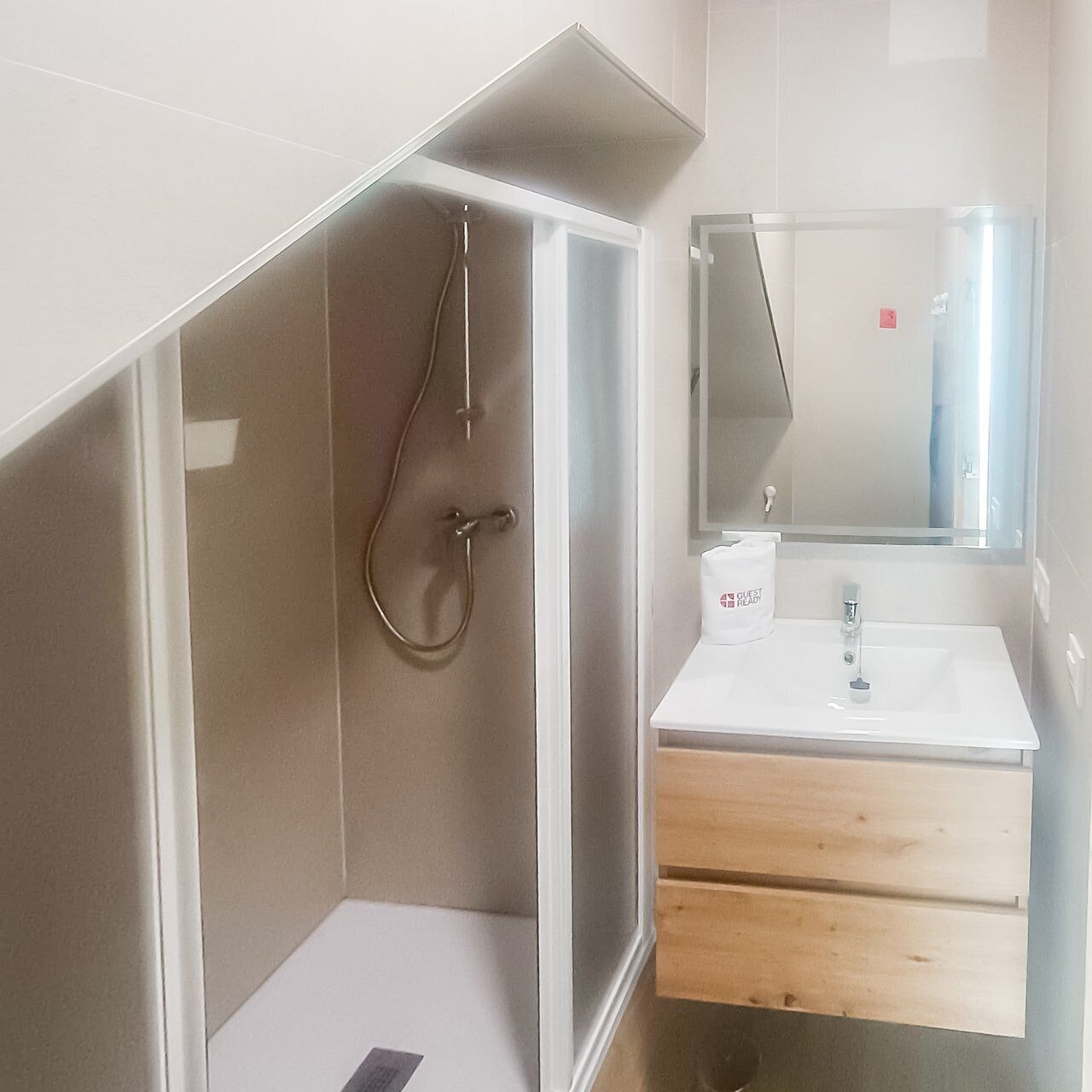 Une salle de bain moderne avec une douche à parois de verre, un lavabo blanc et un meuble-lavabo en bois.