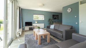 Ein modernes Wohnzimmer mit Fernseher, Sofa, Couchtisch und einem großen Fenster.