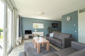 Ein modernes Wohnzimmer mit Fernseher, Sofa, Couchtisch und einem großen Fenster.