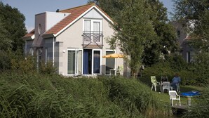 Ein zweigeschossiges Haus mit Balkon, einer kleinen Terrasse und einem Fluss im Vordergrund.