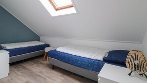 Ein kleiner Raum mit schrägem Dach, zwei Betten, einem kleinen Hocker und einem Korbstuhl.