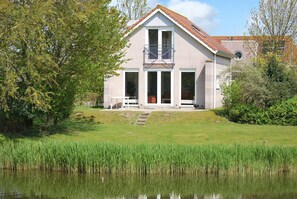Een twee verdiepingen tellend huis met een veranda, een kleine tuin en een vijver ervoor.