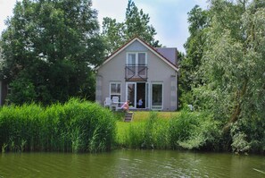A house with a balcony, large windows, and a door leading to a covered porch. - Waterfront Makkum Bungalow With Jetty (Makkum)