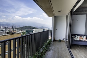 A balcony with a view of a cityscape, a potted plant, and a sofa with decorative pillows. - Puertas del Sol Apartment (Medellín)