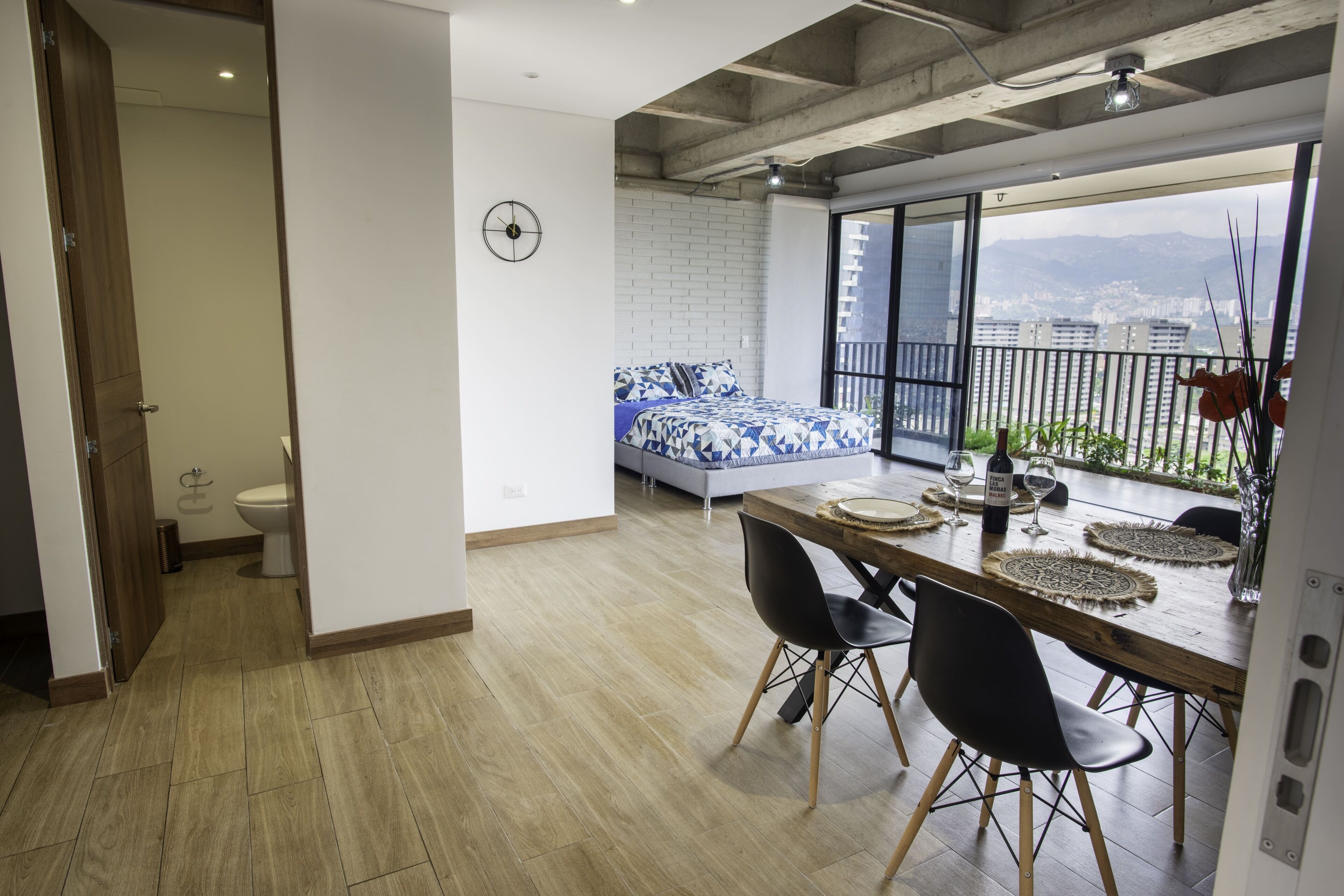 Ein modernes Apartment mit Essbereich, sichtbarer Küche, einem Balkon mit Stadtblick und einem großen Fenster.