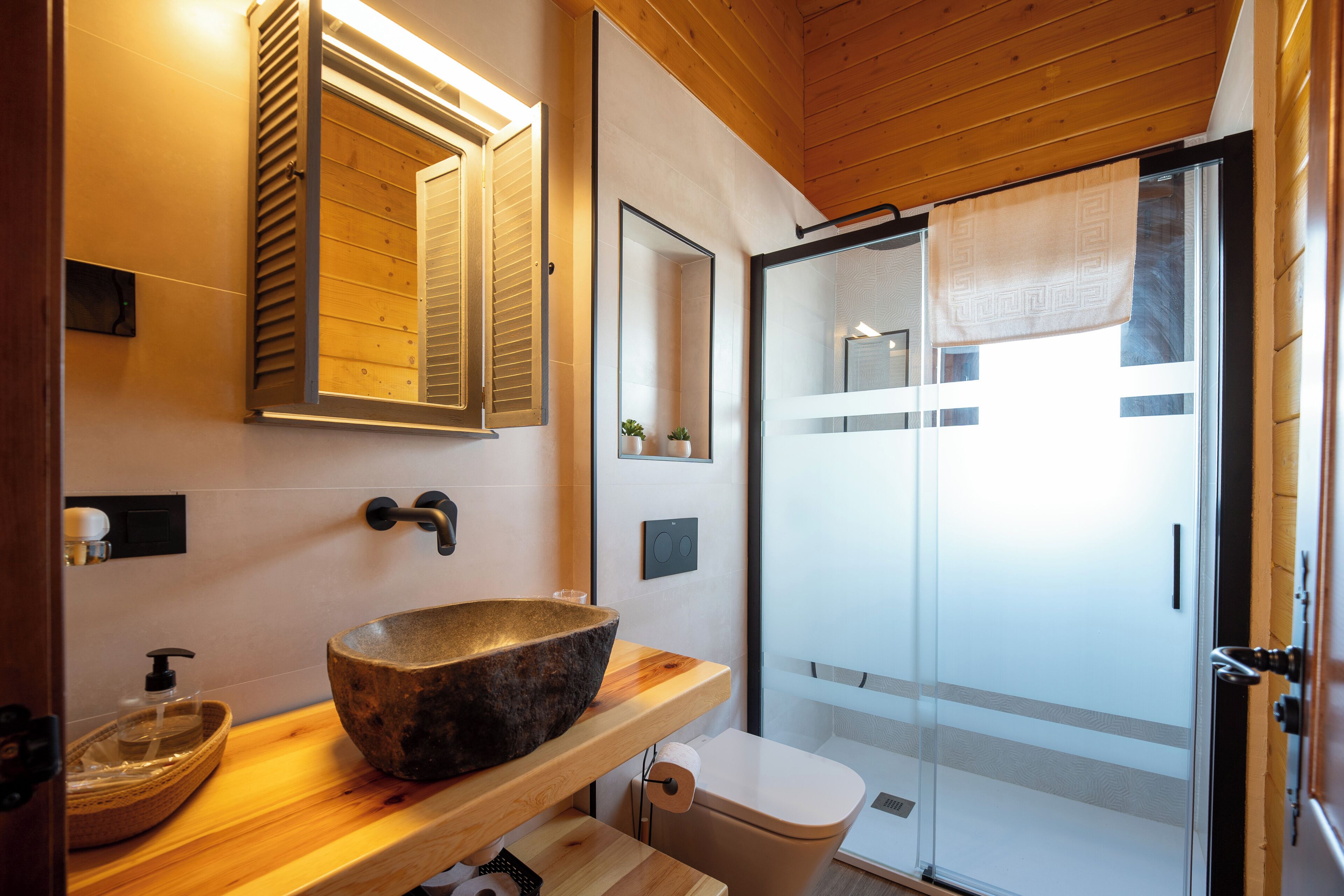Een moderne badkamer met een stenen wasbak, houten planken, een toilet en een douchecabine van glas.