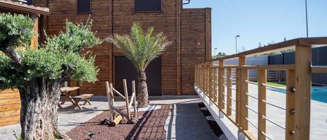 A wooden building with a paved walkway, a pool, and a wooden fence.