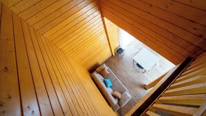 Een houten interieur met een schuine kap, een bank met kussens, en een eettafel met stoelen.