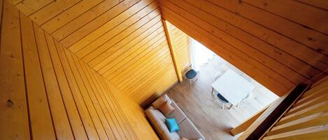 Interior de madera con techo inclinado, un sofá con cojines y una mesa de comedor con sillas.