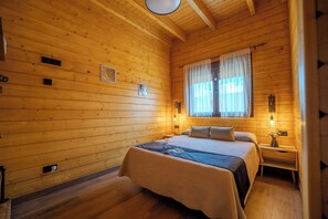 A wooden cabin bedroom with a bed, nightstands, and a window with curtains.