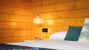 Een houten kamer met een bed, een hanglamp en een kleine tafel met een glazen object erop.