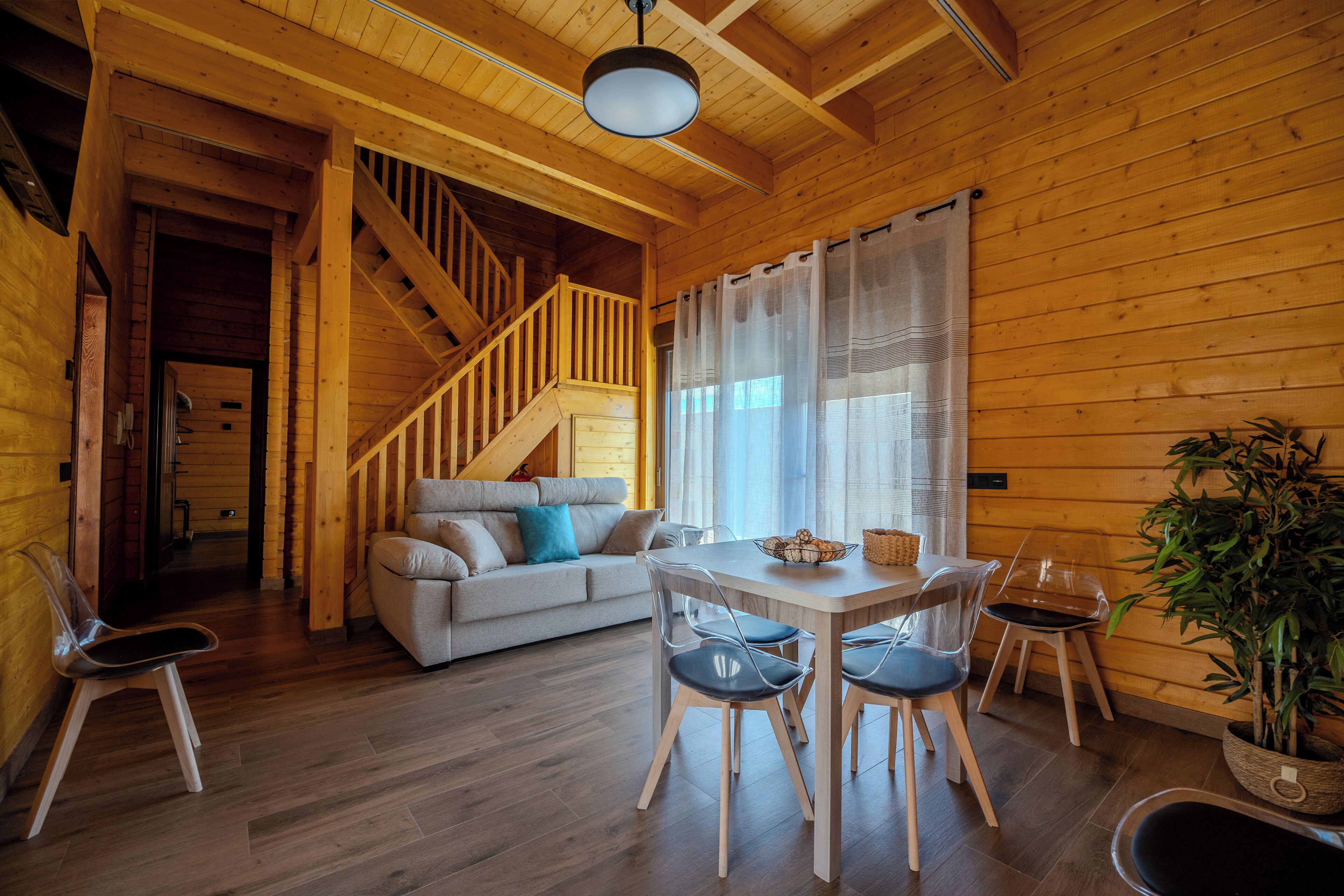Ein Holzblockhaus-Interieur mit Treppe, einer Couch, einem Esstisch mit Stühlen und einer Topfpflanze.