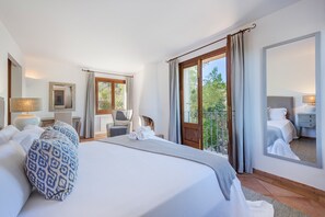 Ein Hotelzimmer mit einem großen Bett, einer Sitzecke mit Sessel und Tisch, einem Balkon mit Blick und einem großen Spiegel.