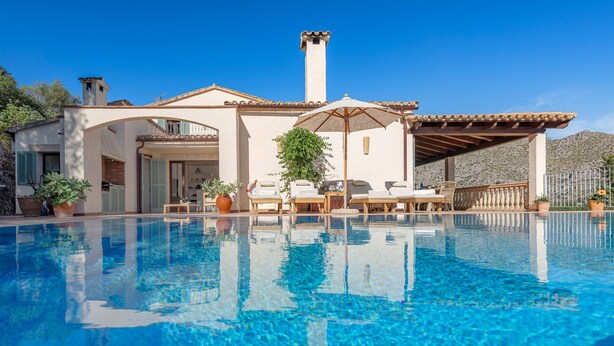 Uma área à beira da piscina com piscina azul cristalina, espreguiçadeiras e um pérgola.